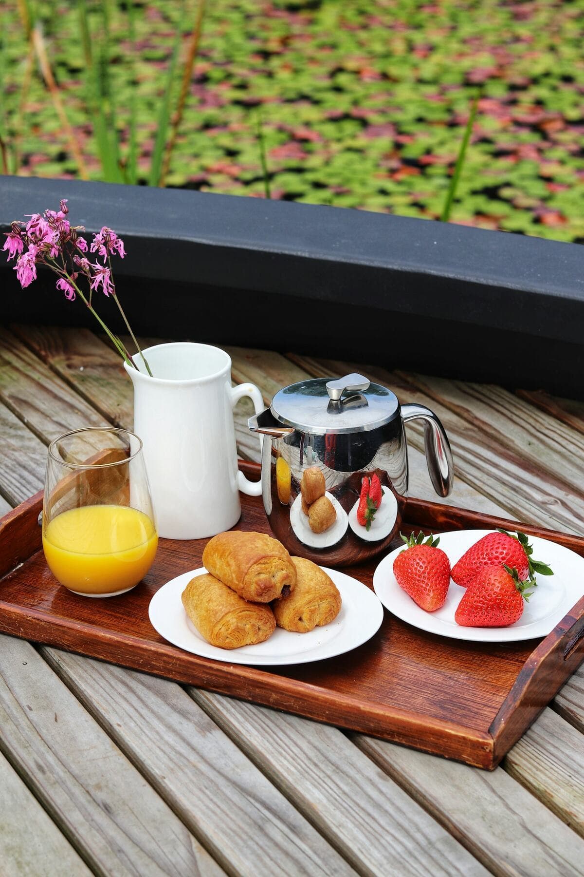A breakfast tray with pastries, fruit and orange juice on a wooden deck